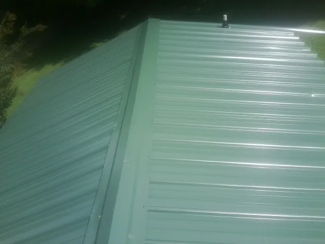 New green metal panels meeting at the ridge of a roof — Flat Roof Repair work by our crew in Trumbull