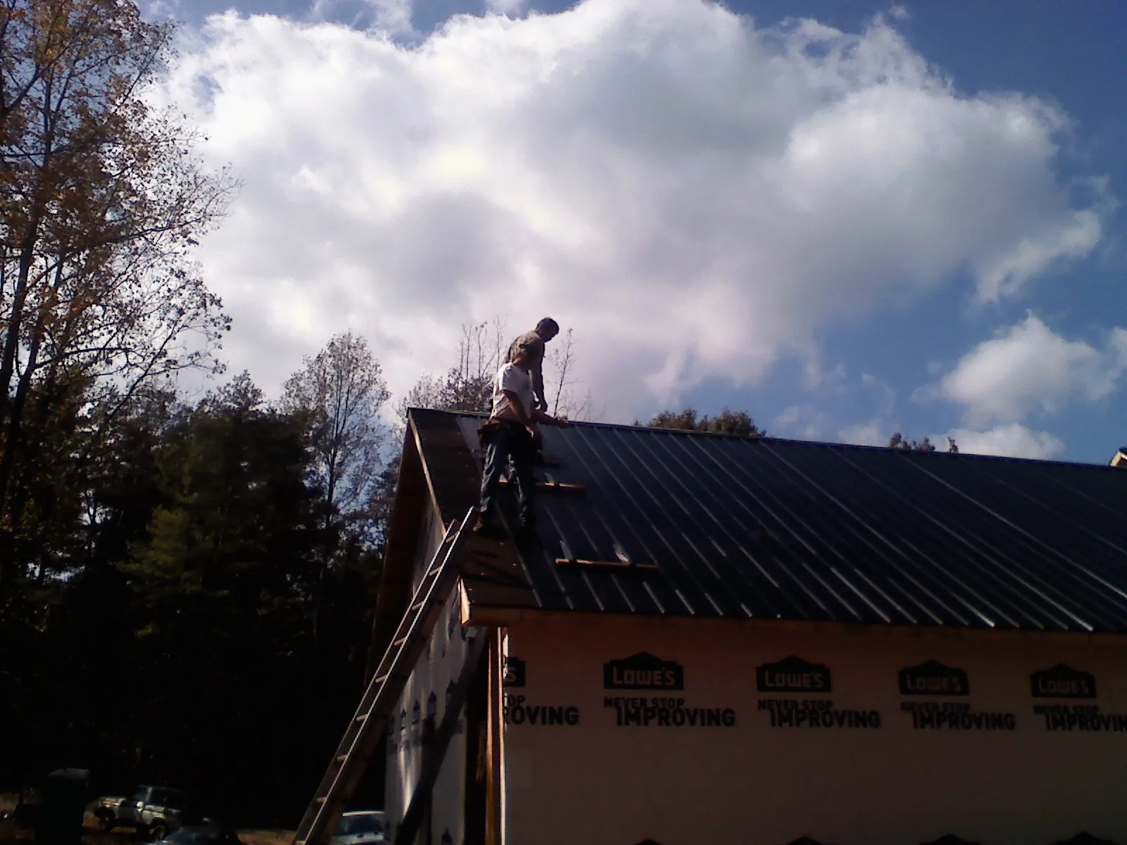 Roofer fastening dark metal panels high against a cloudy sky, from a Roof Inspection job in Trumbull