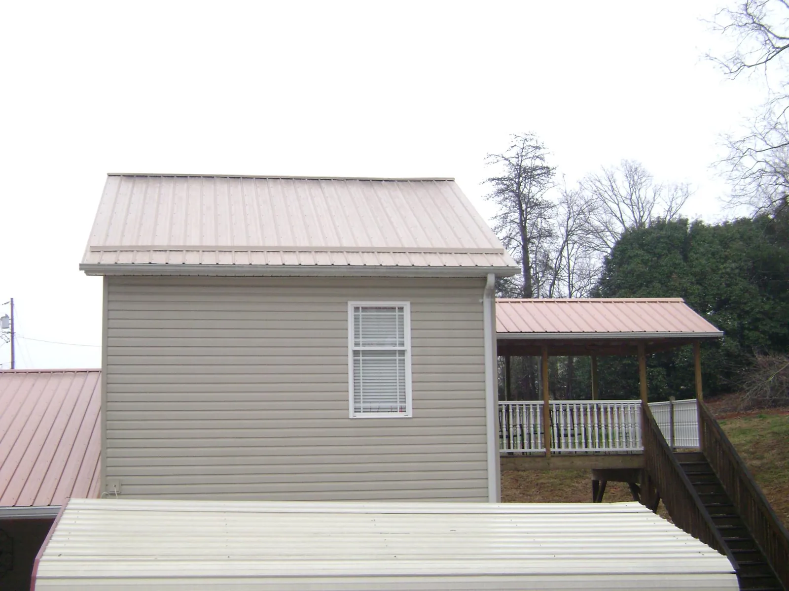 Tan metal roofs on a two story addition and attached porch, from a Roof Replacement job in Trumbull